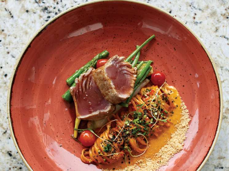 Seared tuna with Thai curry linguini and sautéed green beans served on a red speckled plate.