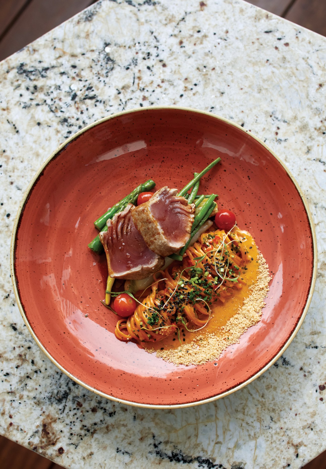 Seared tuna with Thai curry linguini and sautéed green beans served on a red speckled plate.