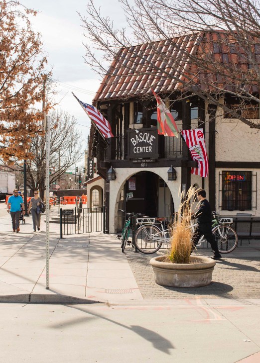 Boise's Basque Center building with traditional architecture, American and Basque flags, cyclists, and pedestrians on the street.