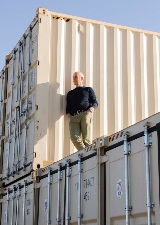 Pete Gombert, co-founder of IndieDwell, standing on a modular home container against a clear blue sky.