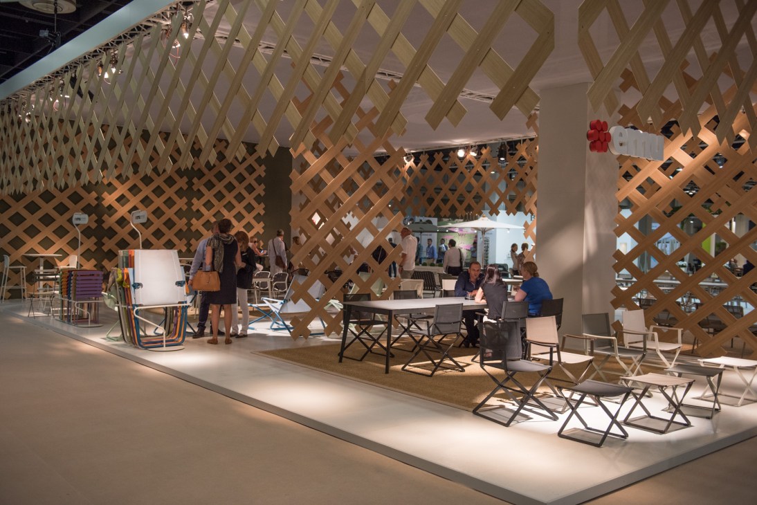 Emu stand at Spoga+Gafa garden fair featuring chairs, tables, and wooden lattice panels with visitors.