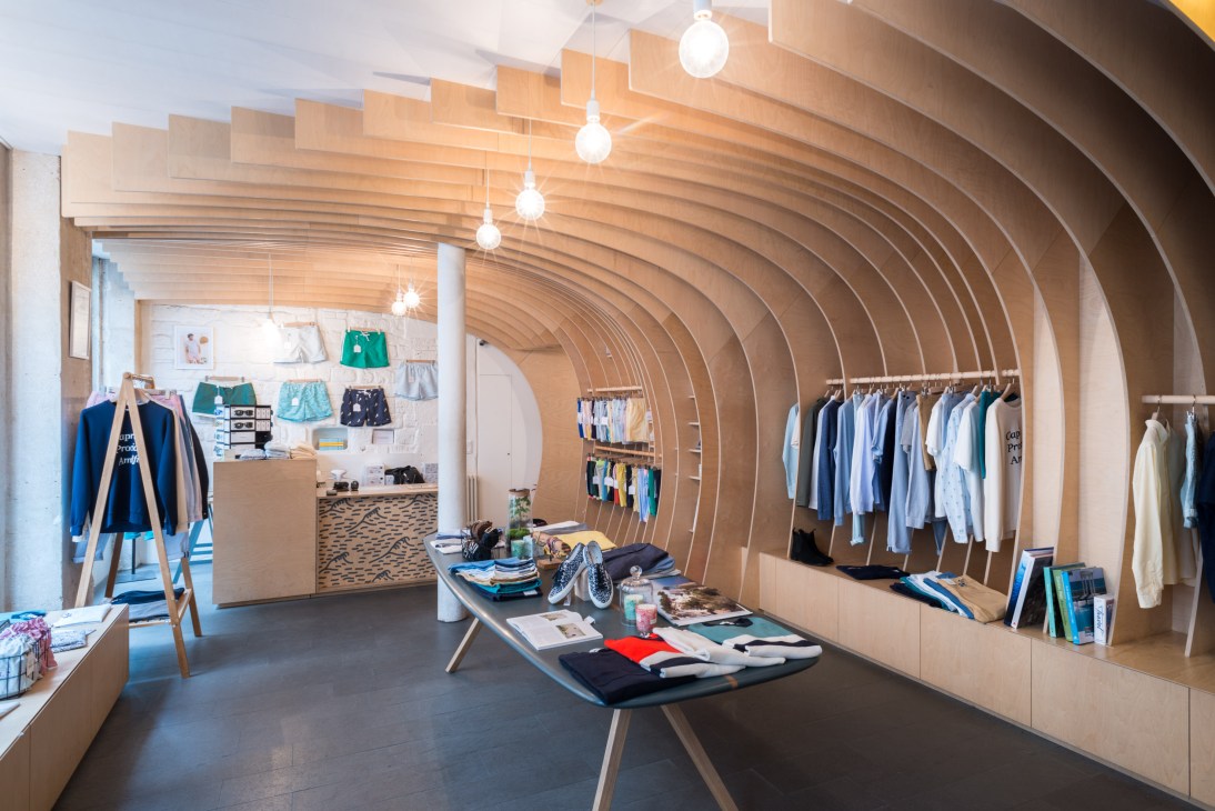 Interior of Cuisse de Grenouille shop in Paris with curved wooden ceiling, pendant lights, clothing racks, and display tables.