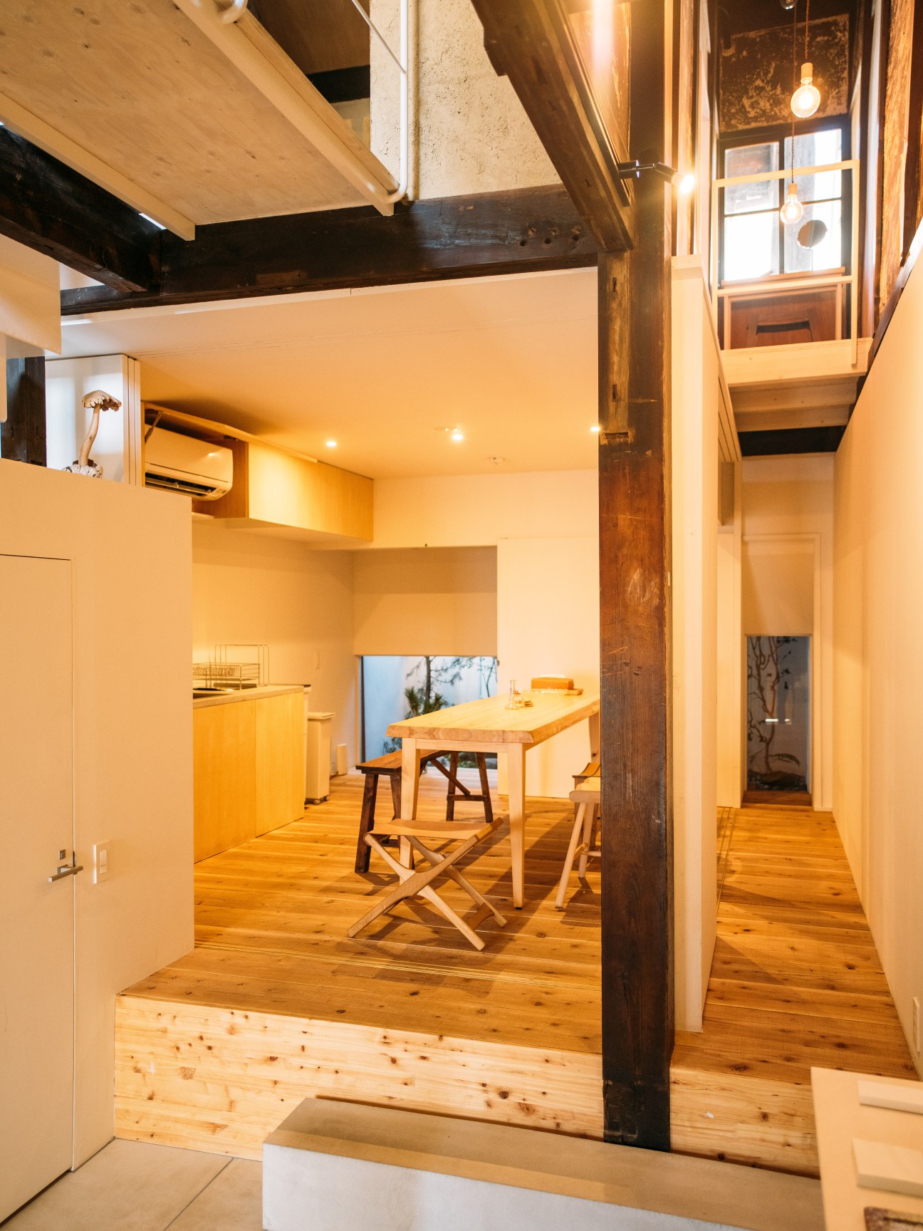 Open kitchen-dining room with wooden table, natural wood flooring, and exposed dark ceiling beams in renovated machiya house.