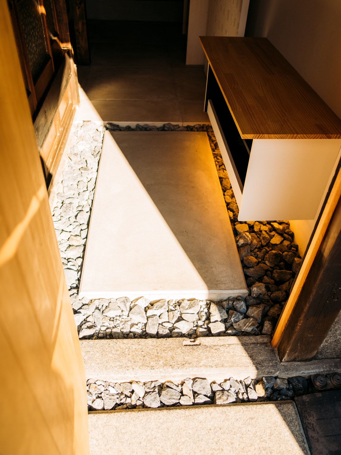 Entrance to A Day in Khaki guesthouse with shoe removal area, wooden benches, and gravel flooring.