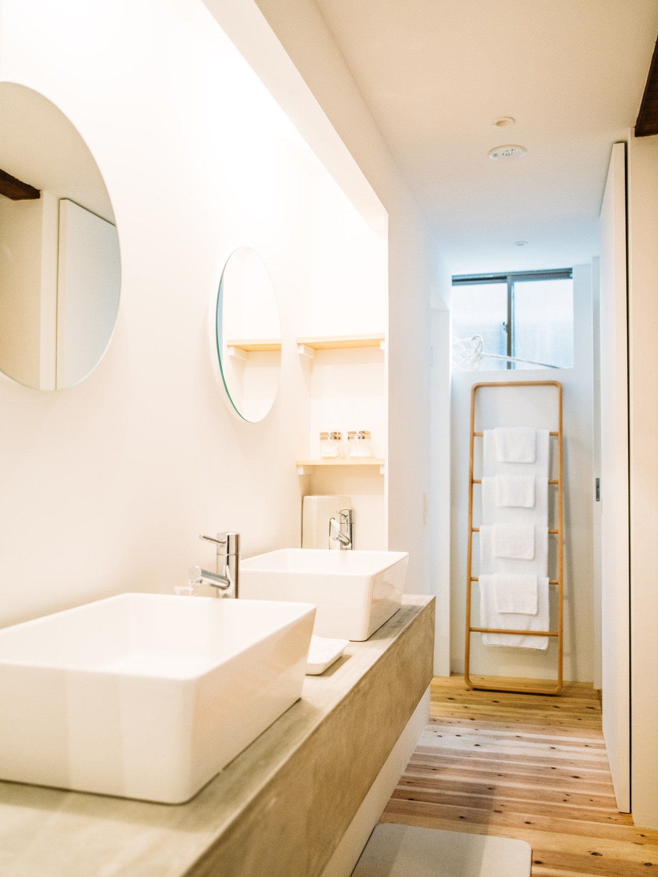 Modern bathroom with dual white vessel sinks, wooden vanity, round mirrors, and wooden towel ladder in renovated Kyoto machiya guesthouse.