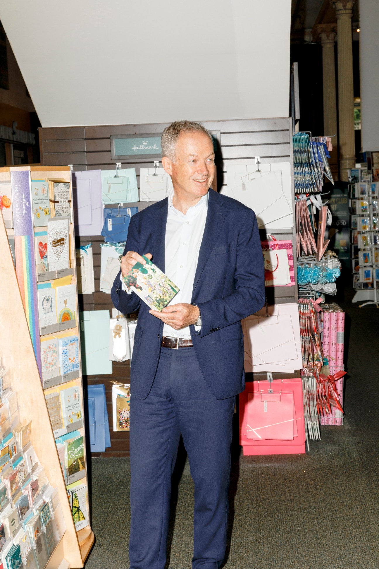 Man in navy suit holding greeting card while browsing card display in retail store