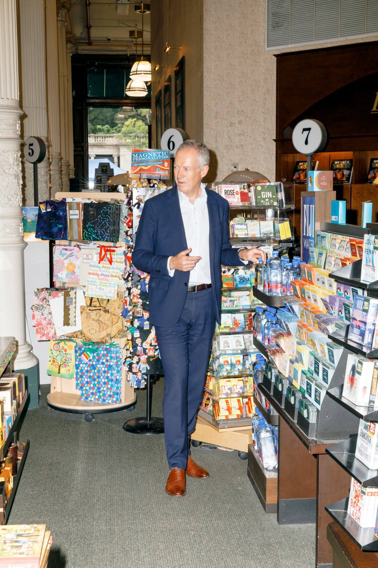 Man in navy suit browsing books in bookstore aisle with numbered sections and display racks