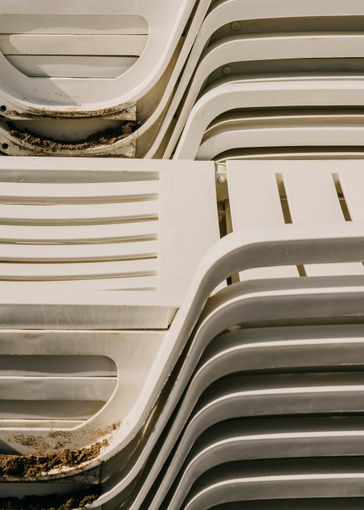 Stacked white and beige plastic beach loungers with some showing wear and dirt accumulation.