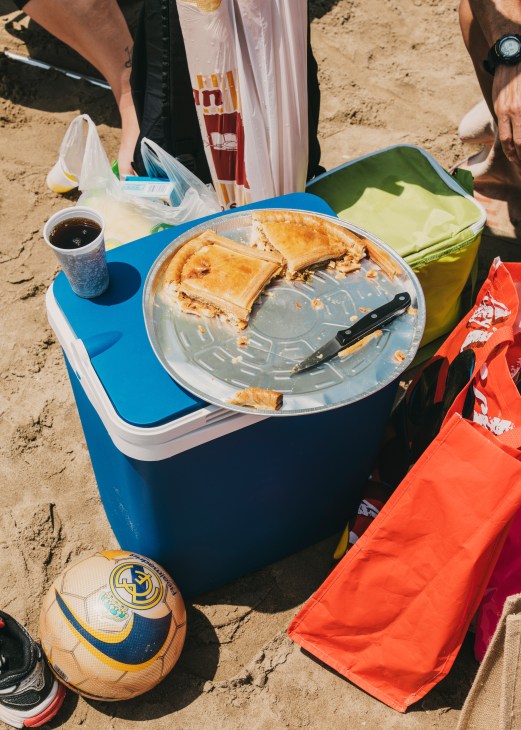 Picnic lunch on a blue cooler at Valencia beach with empanadas, a knife, and a soft drink.