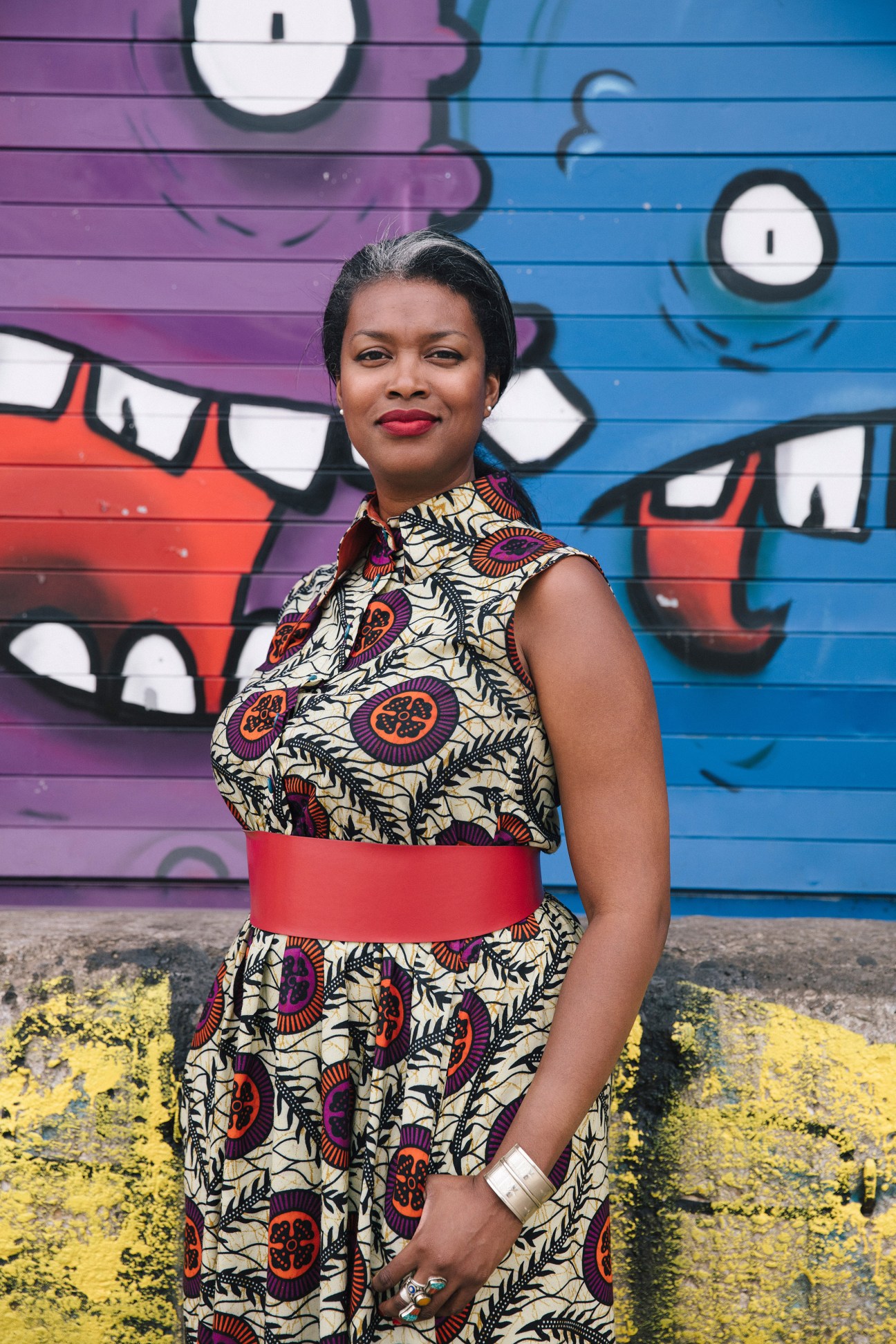 Woman in patterned dress with red belt standing in front of colorful street mural