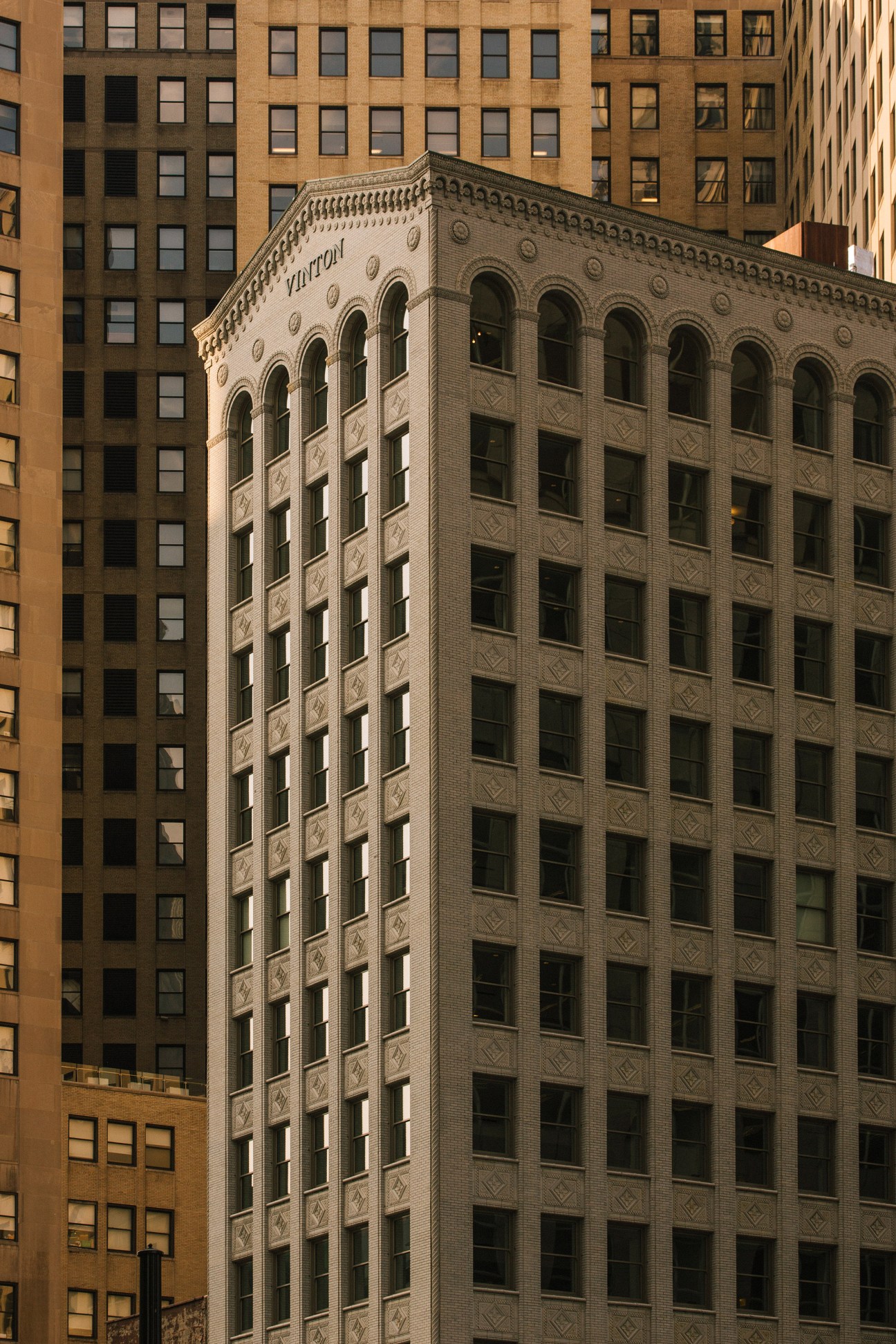 Historic brick building with arched windows surrounded by taller modern office buildings in downtown Detroit.