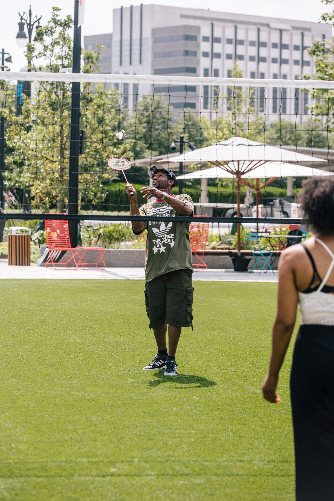 People playing badminton at Beacon Park in downtown Detroit with modern high-rise buildings in the background.