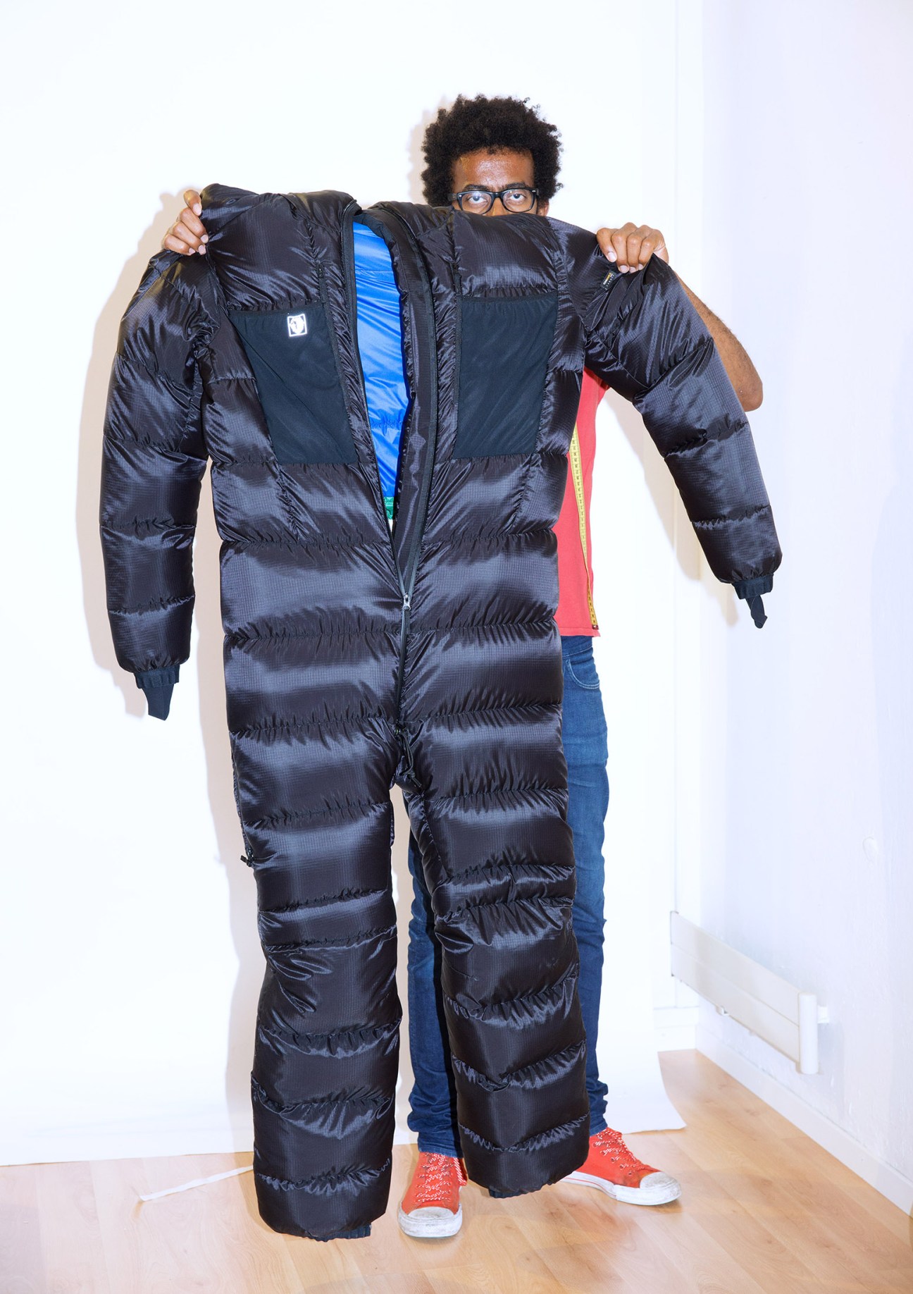Person holding up a black quilted full-body climbing suit designed for Mount Everest expeditions.
