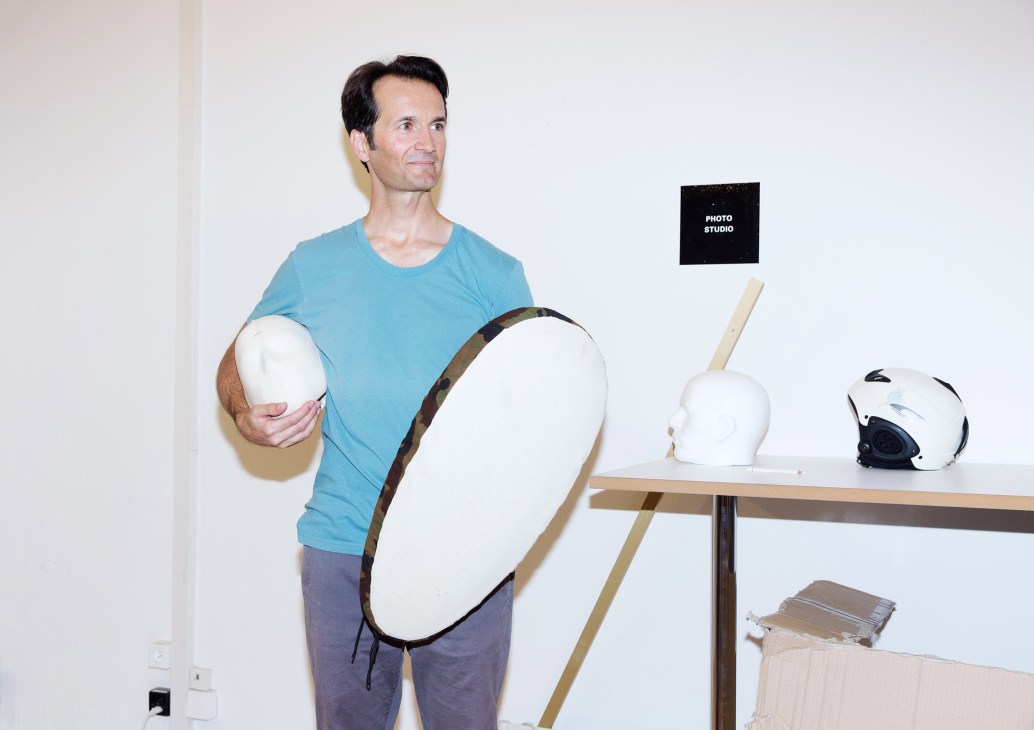 Thomas Deutschenbaur holds testing equipment in DNS studio with helmets and samples on table