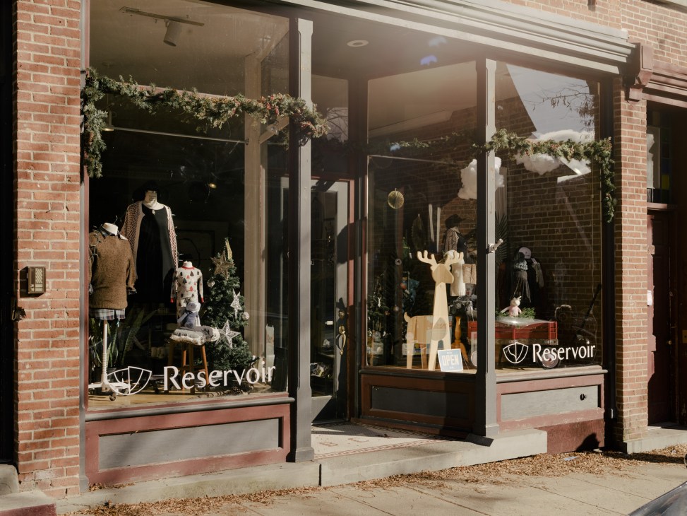 Reservoir storefront window display with clothing, plants, and merchandise on red-brick Main Street.