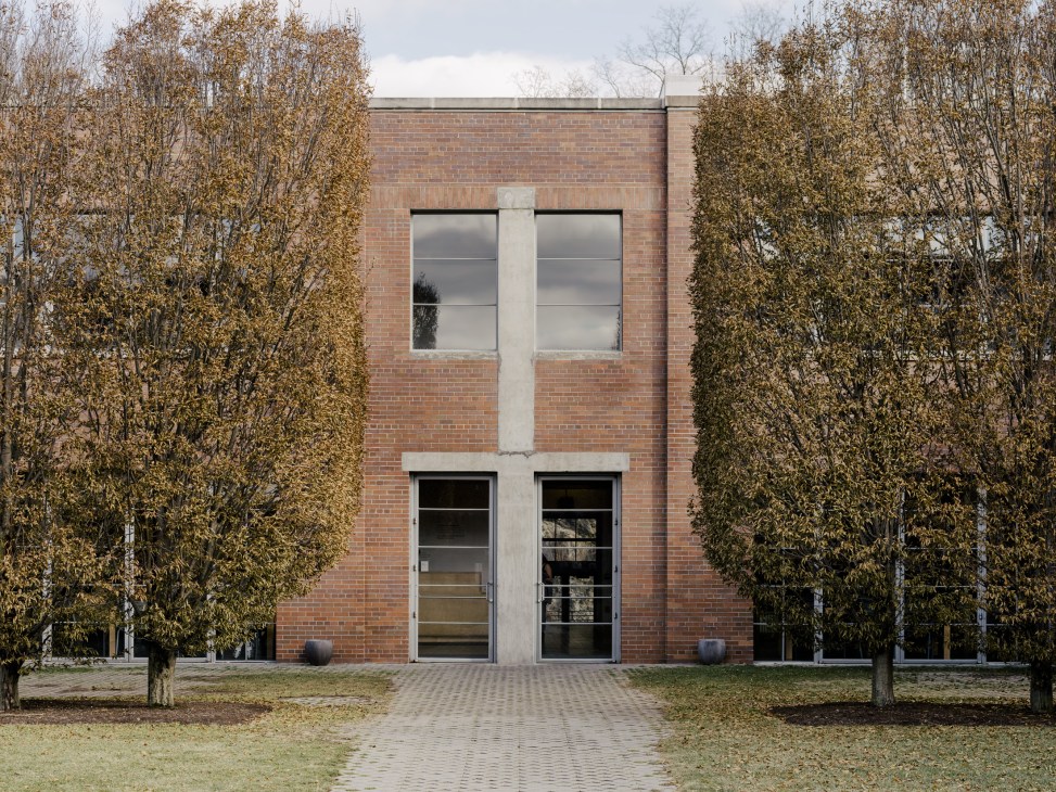 Modern brick building with large windows flanked by bare trees in autumn.