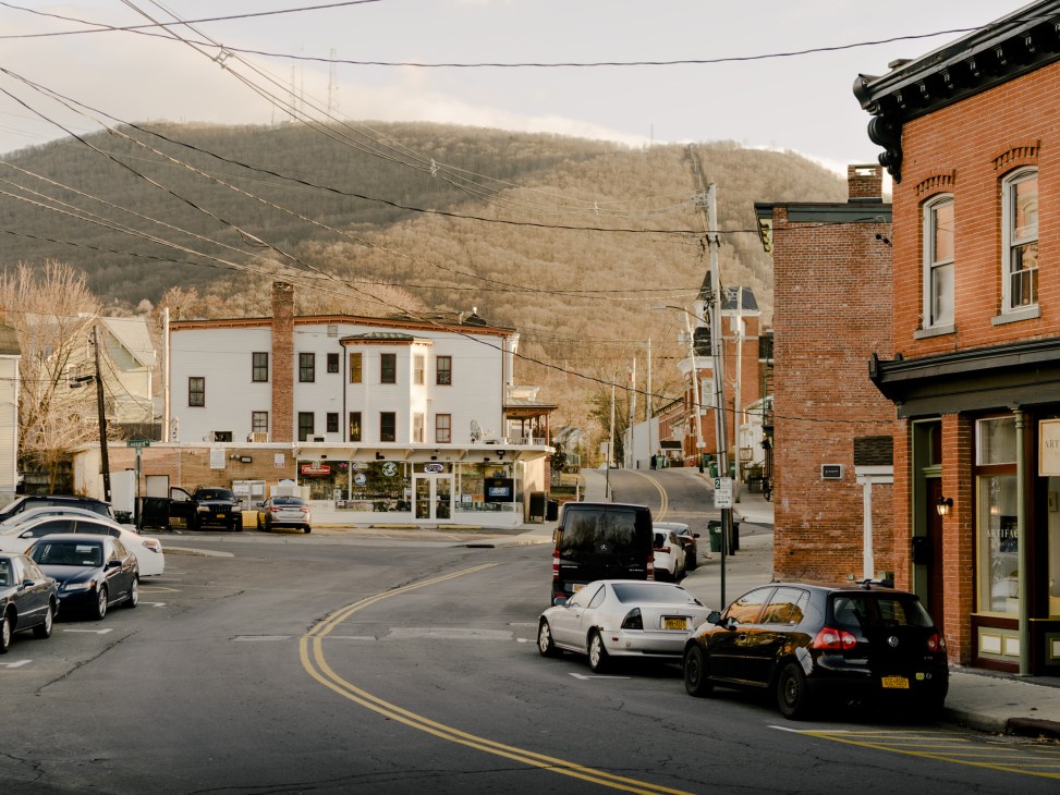 Beacon's Main Street lined with brick buildings and parked cars, with forested mountains visible in the background.
