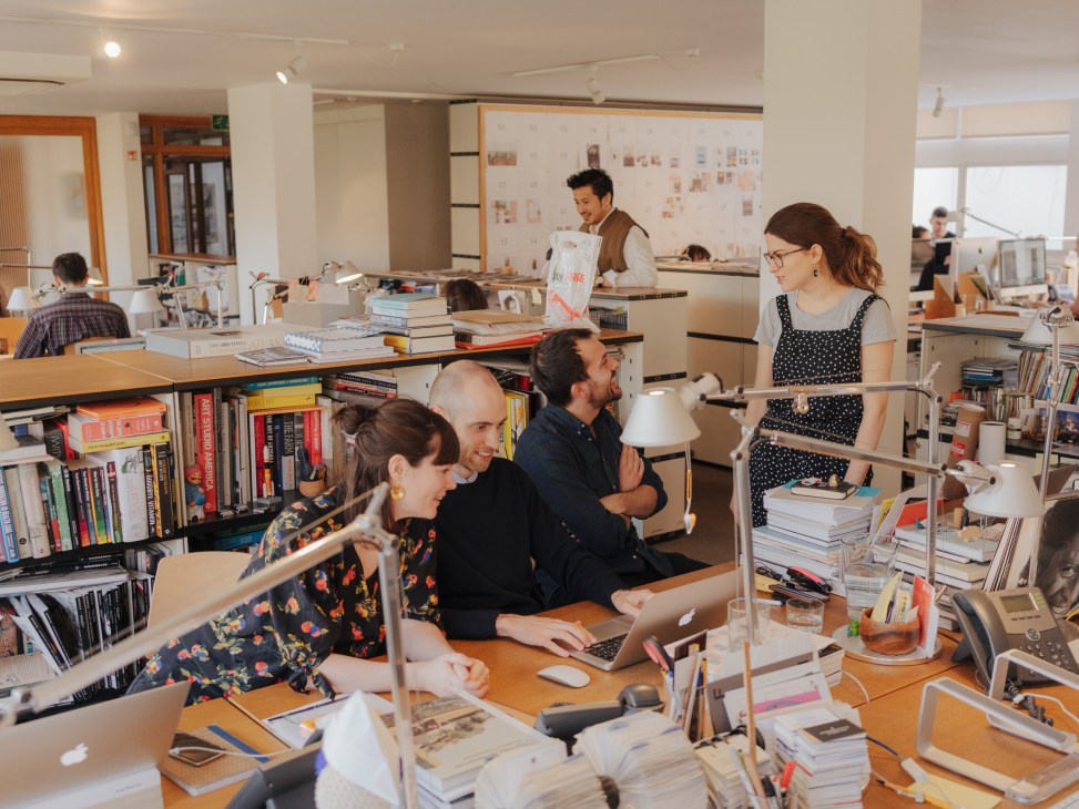 Monocle editors and staff collaborate at desks in an open office space surrounded by books and design materials.