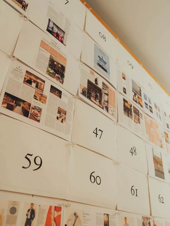 Magazine pages numbered 47-62 pinned to a wall showing layout designs with text and photographs.