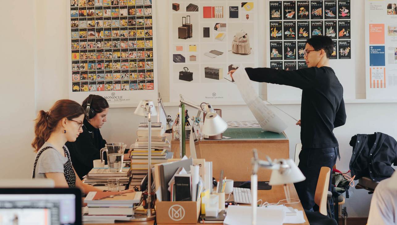Monocle staff members at desks reviewing magazine layouts and running order in office with design boards on walls.