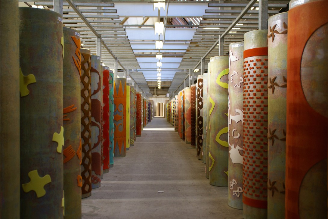 Rolls of colorful wax-printed fabric lined up in a factory corridor with industrial lighting.
