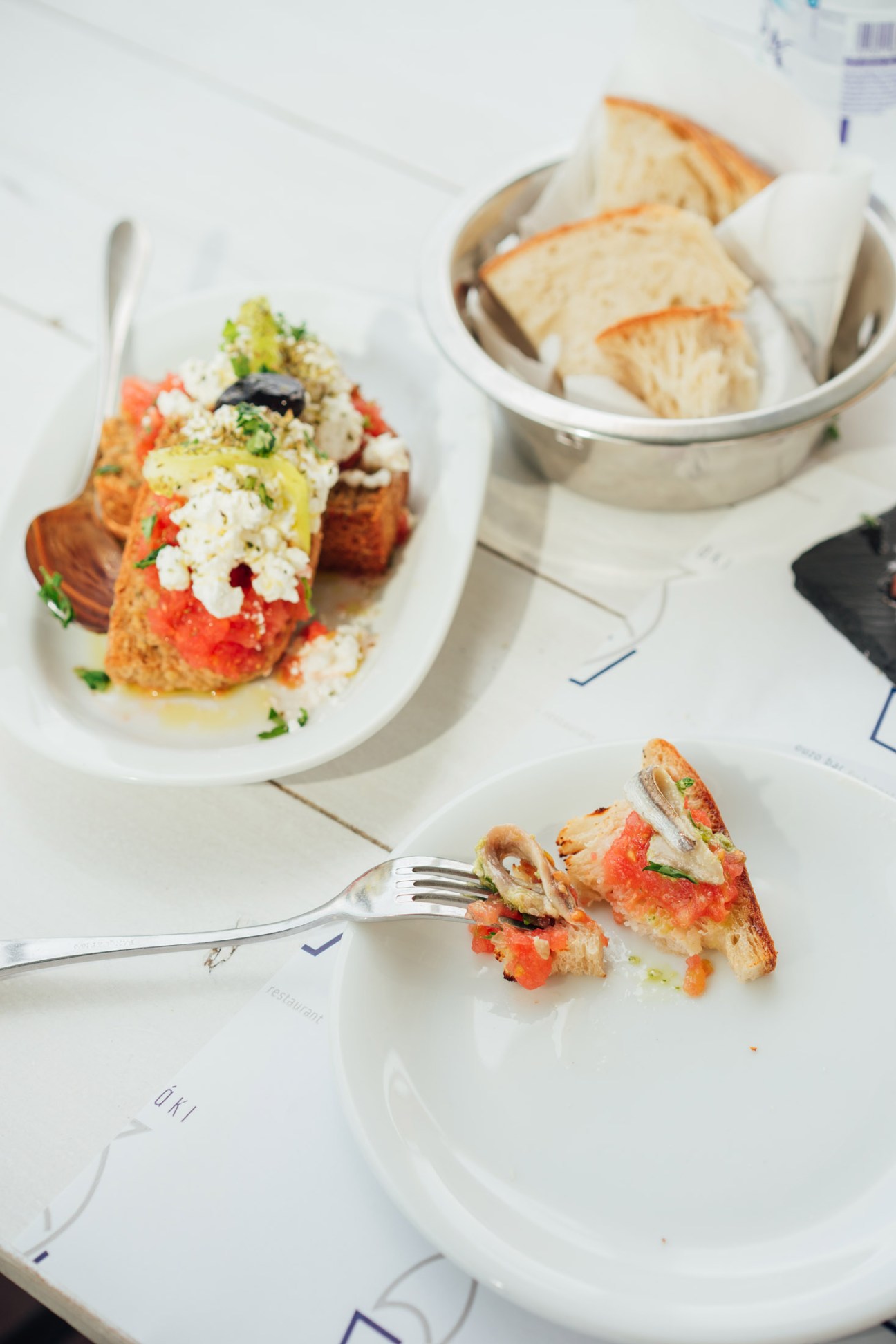 Meze appetizers at Psaraki restaurant including tomato and feta topped fish with bread basket and fork.