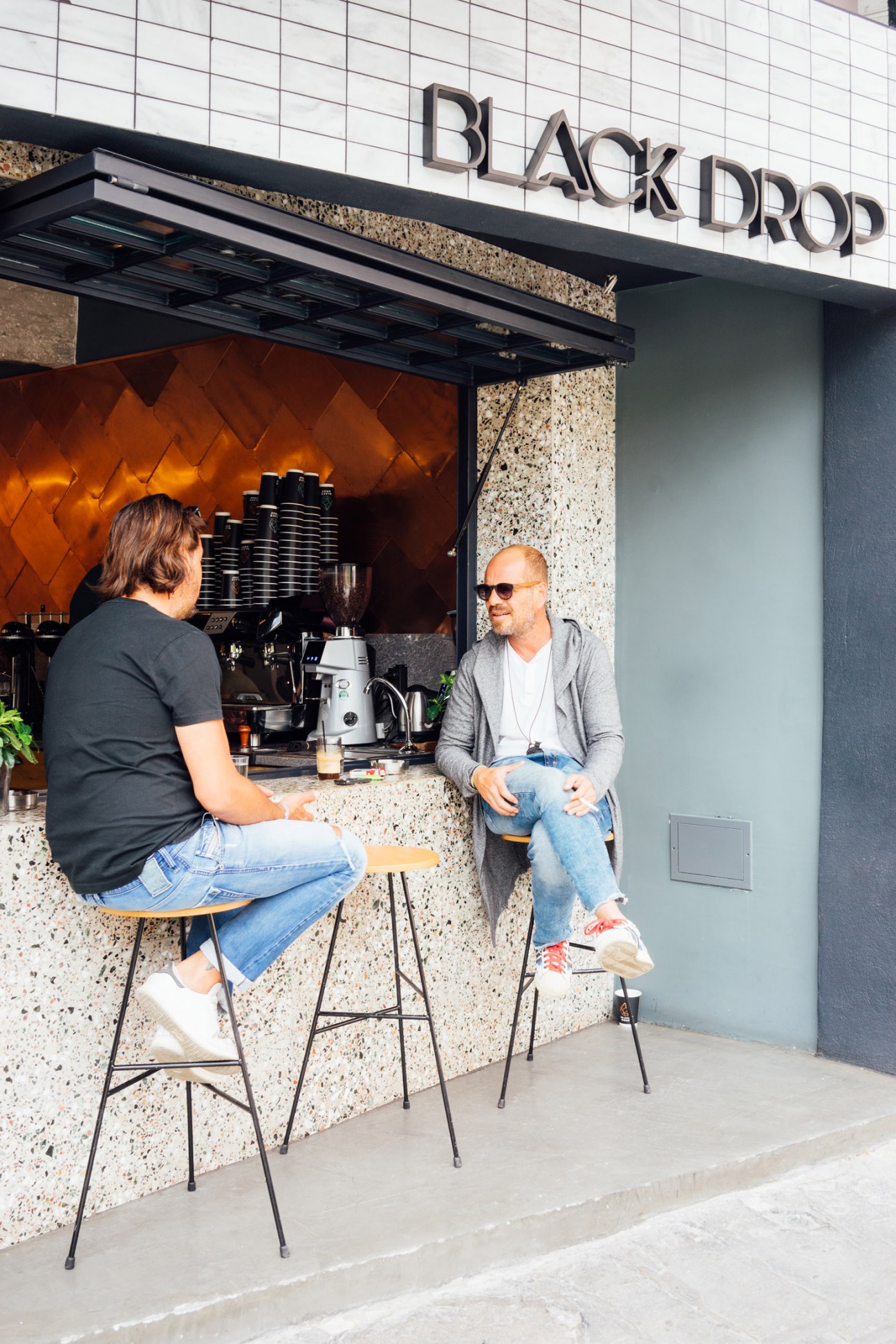 Two people seated at the counter of Black Drop coffee shop in Kavala, Greece.