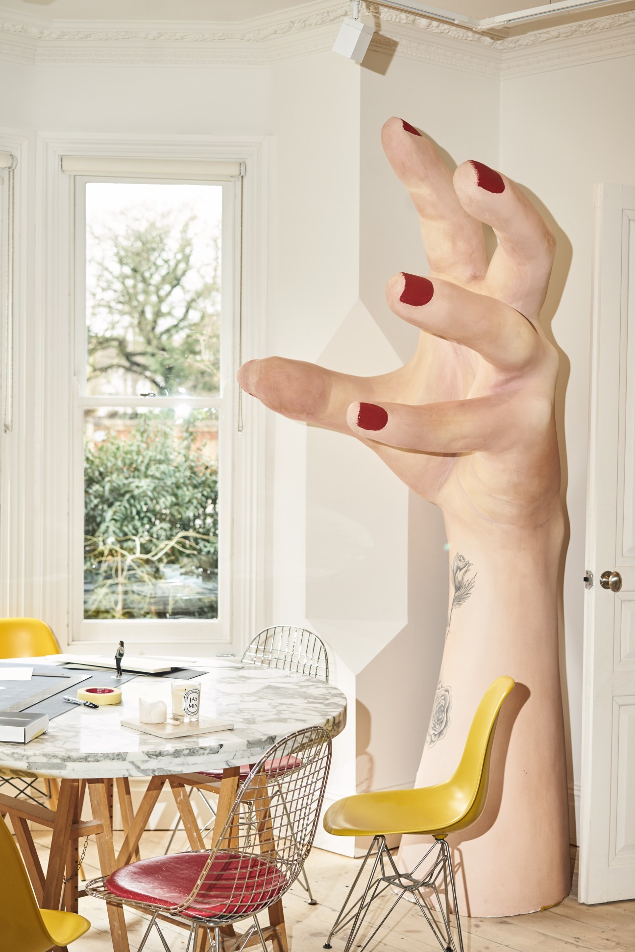 Oversized sculptural hand with burgundy nail polish reaching across a minimalist interior space.