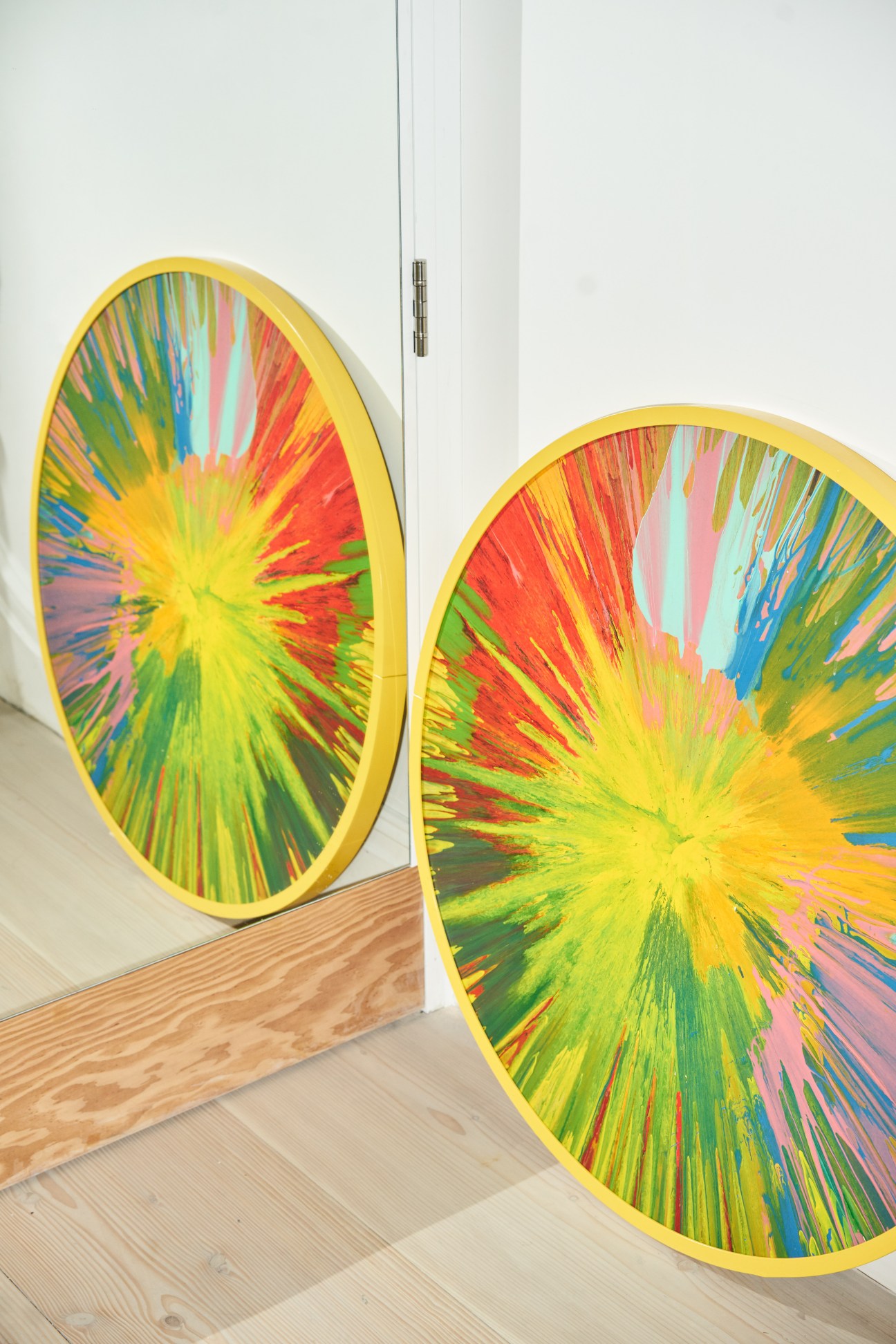 Two large circular artworks with yellow frames featuring radiating multicolored streaks in a gallery space.