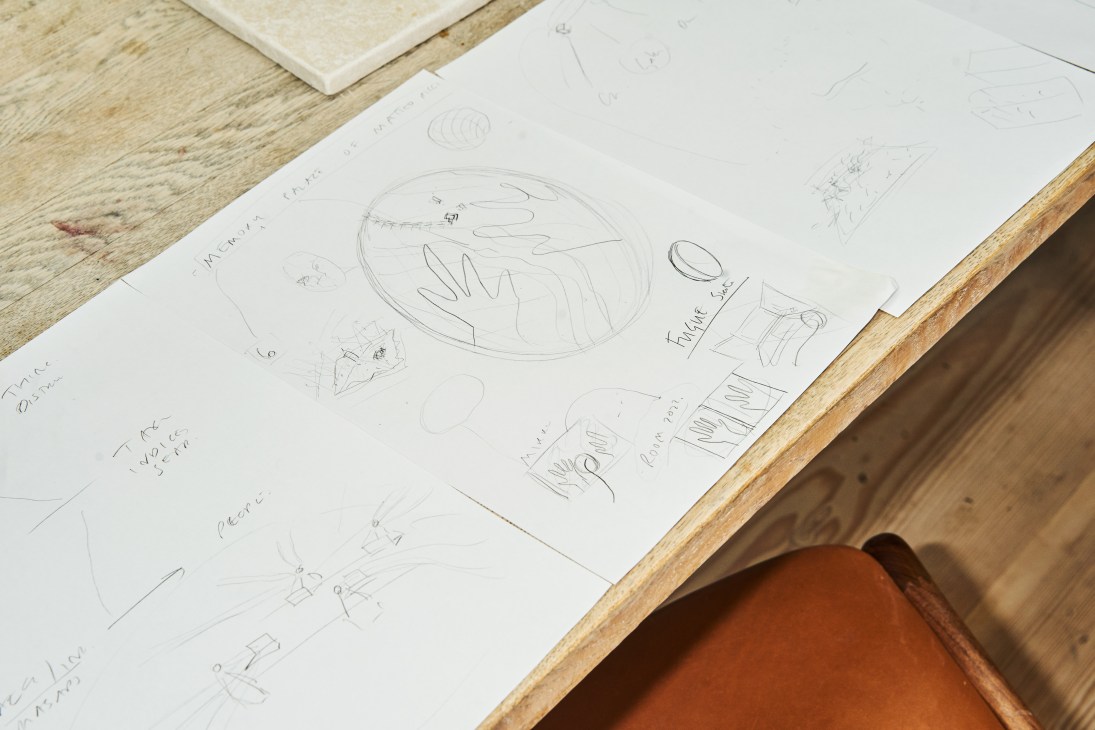 Es Devlin's sketches and drawings spread across a wooden table with handwritten notes and design details.