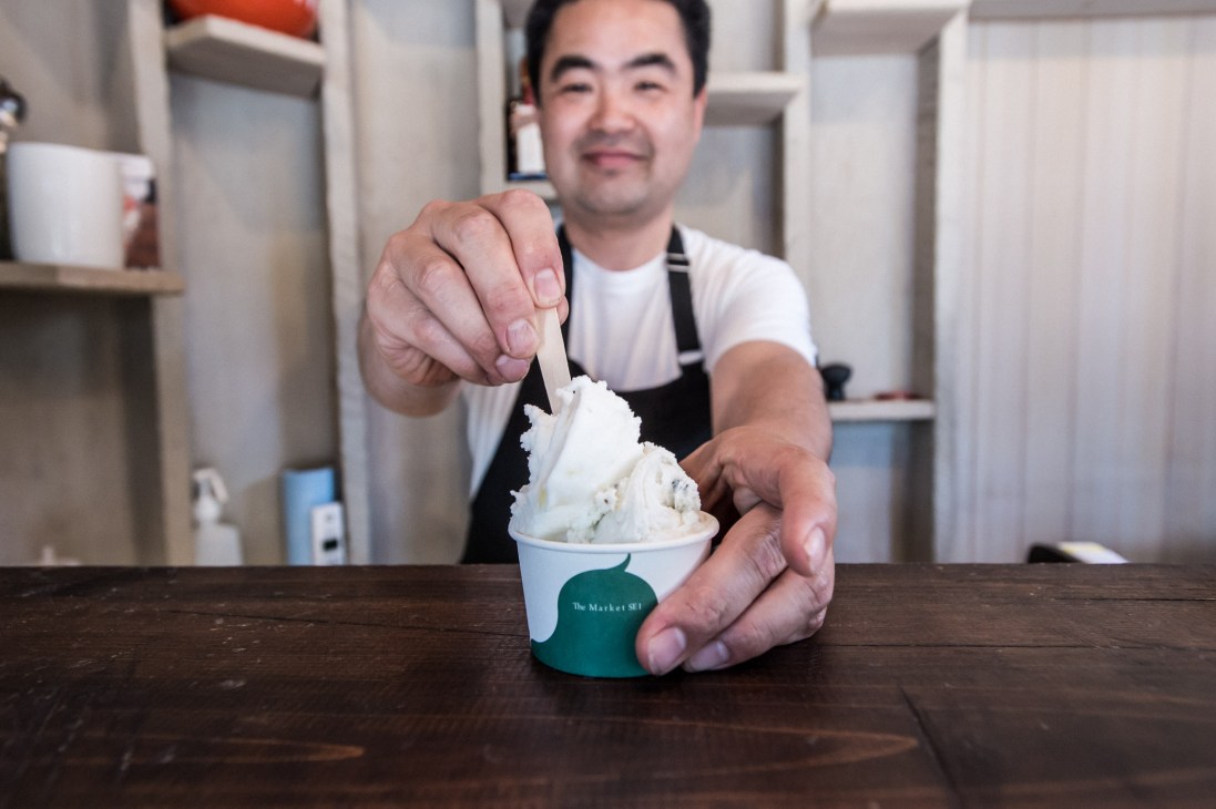 Man in apron scoops white ice cream from a cup branded with The Market SE1 logo.