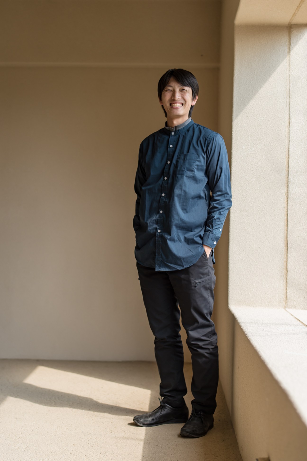 Takanobu Yoshida, general manager of Log hotel, stands smiling in a minimalist corridor.