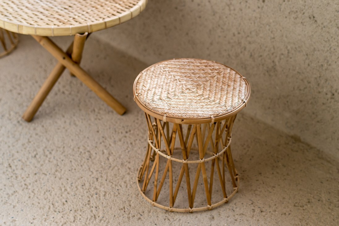 Handcrafted wooden stool with woven rattan seat and geometric bamboo base on concrete floor.