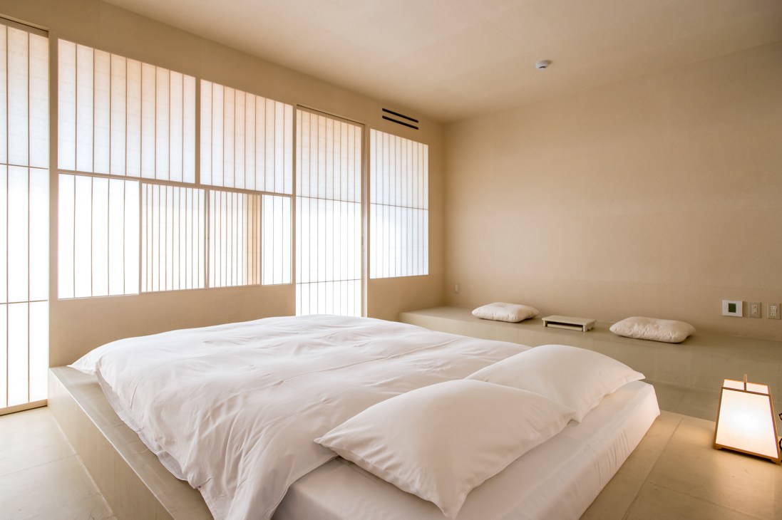 Minimalist bedroom at Lantern Onomichi Garden hotel with white bedding, washi paper screens, and warm beige walls.