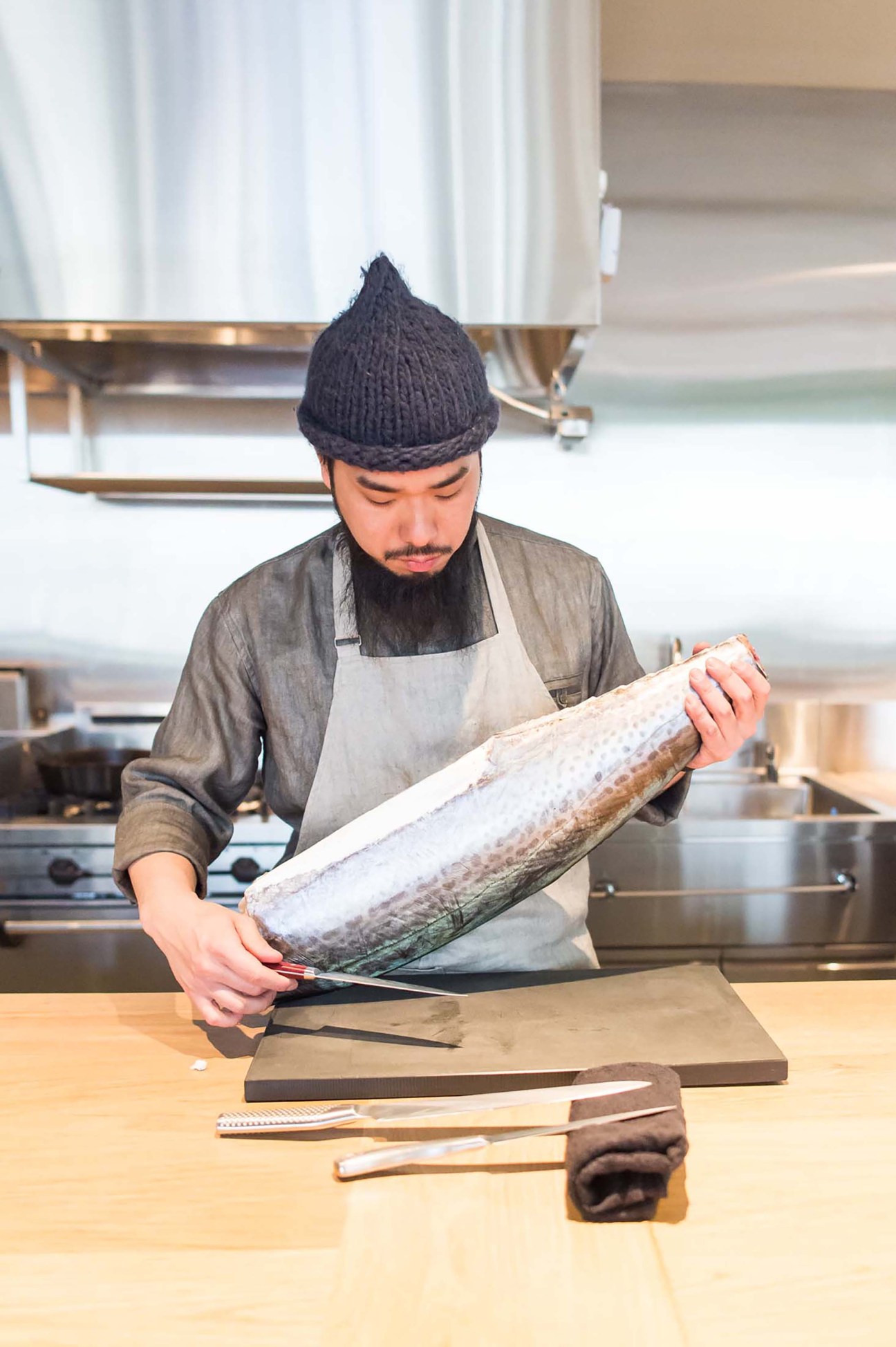 Chef in knit cap and apron preparing large fish on cutting board in professional kitchen