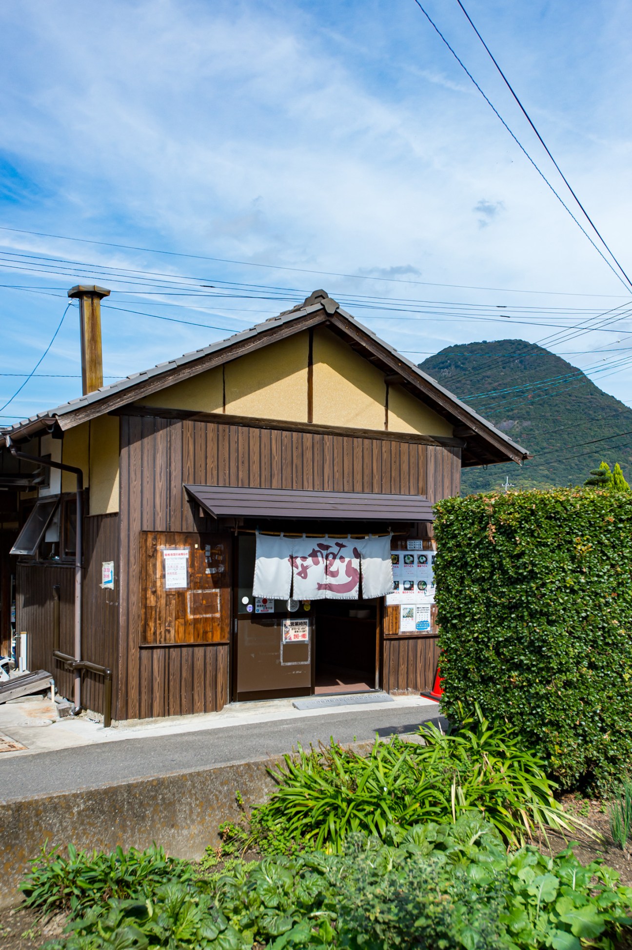 Traditional wooden udon restaurant exterior with noren curtain and mountain backdrop in rural Japan