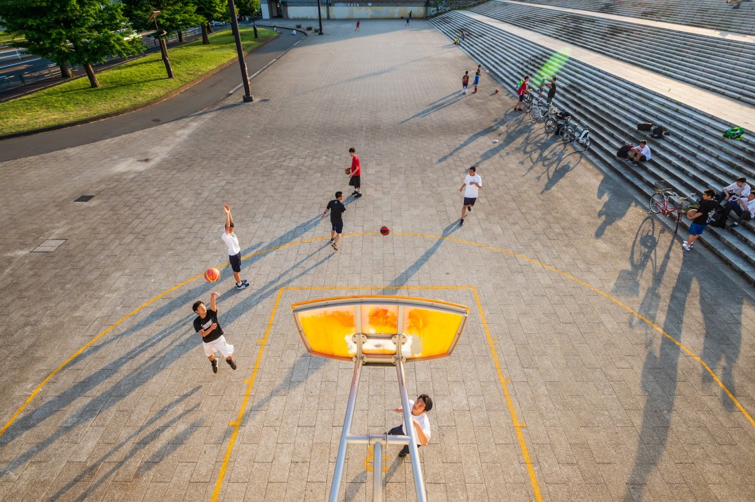 Overhead view of people playing basketball on a court with yellow markings in an urban park.