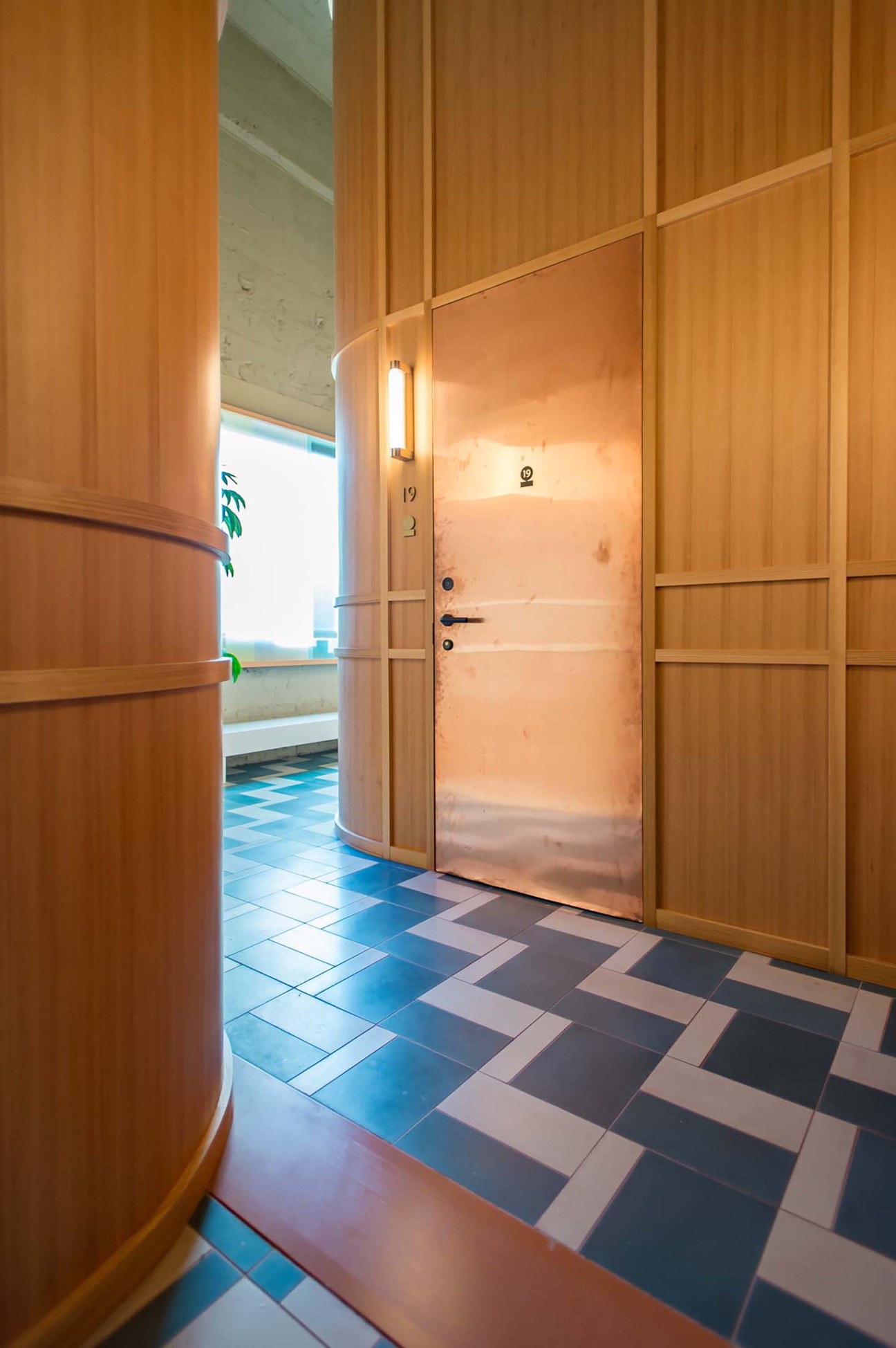 Modern corridor with warm wood paneling, geometric blue and white floor tiles, and door number 19