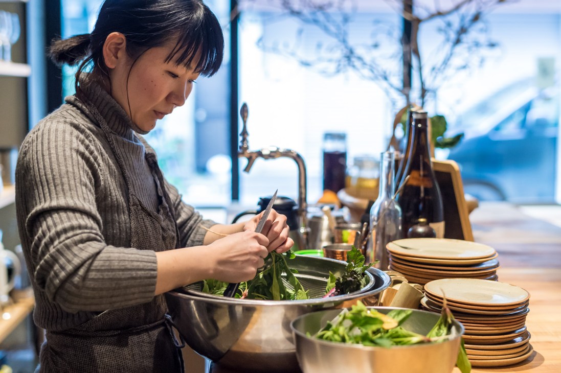 Woman preparing fresh greens in a metal bowl at The Blind Donkey restaurant in Tokyo.