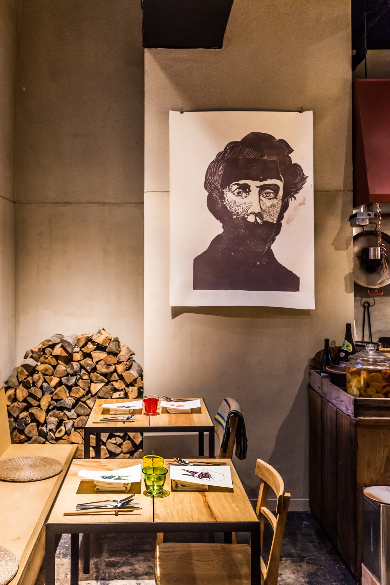 The Blind Donkey restaurant interior with wooden tables, stacked firewood, and portrait artwork on wall.