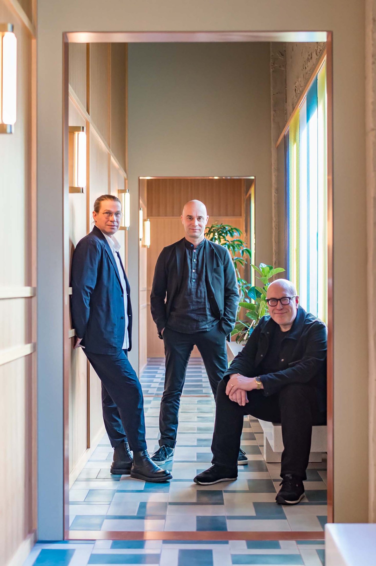 Three men standing in a modern hotel corridor with geometric patterned flooring and warm lighting