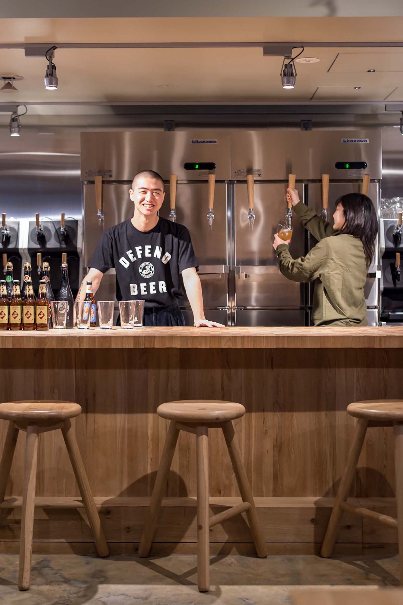Bartender in black shirt behind wooden bar counter serving customer at Brooklyn Brewery taproom