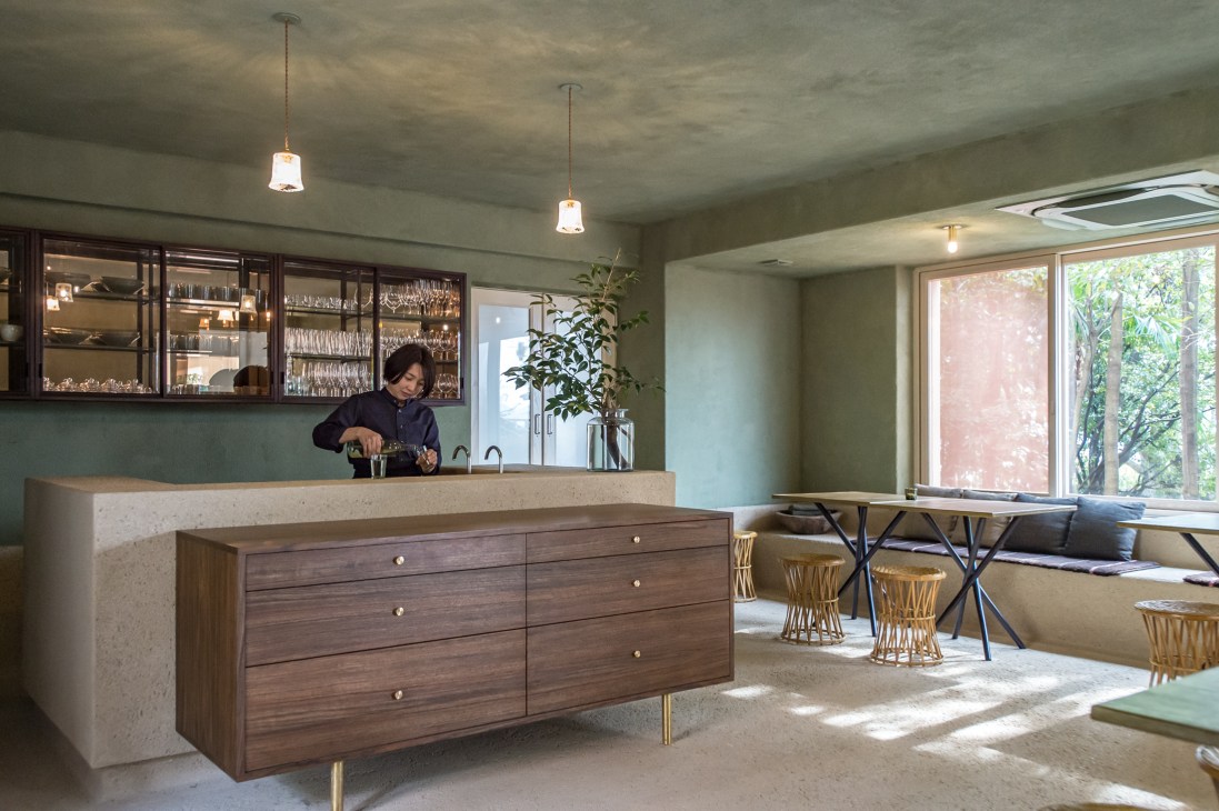 Server pouring drinks behind counter in Lantern Onomichi Garden hotel dining room with green walls and wooden furniture.