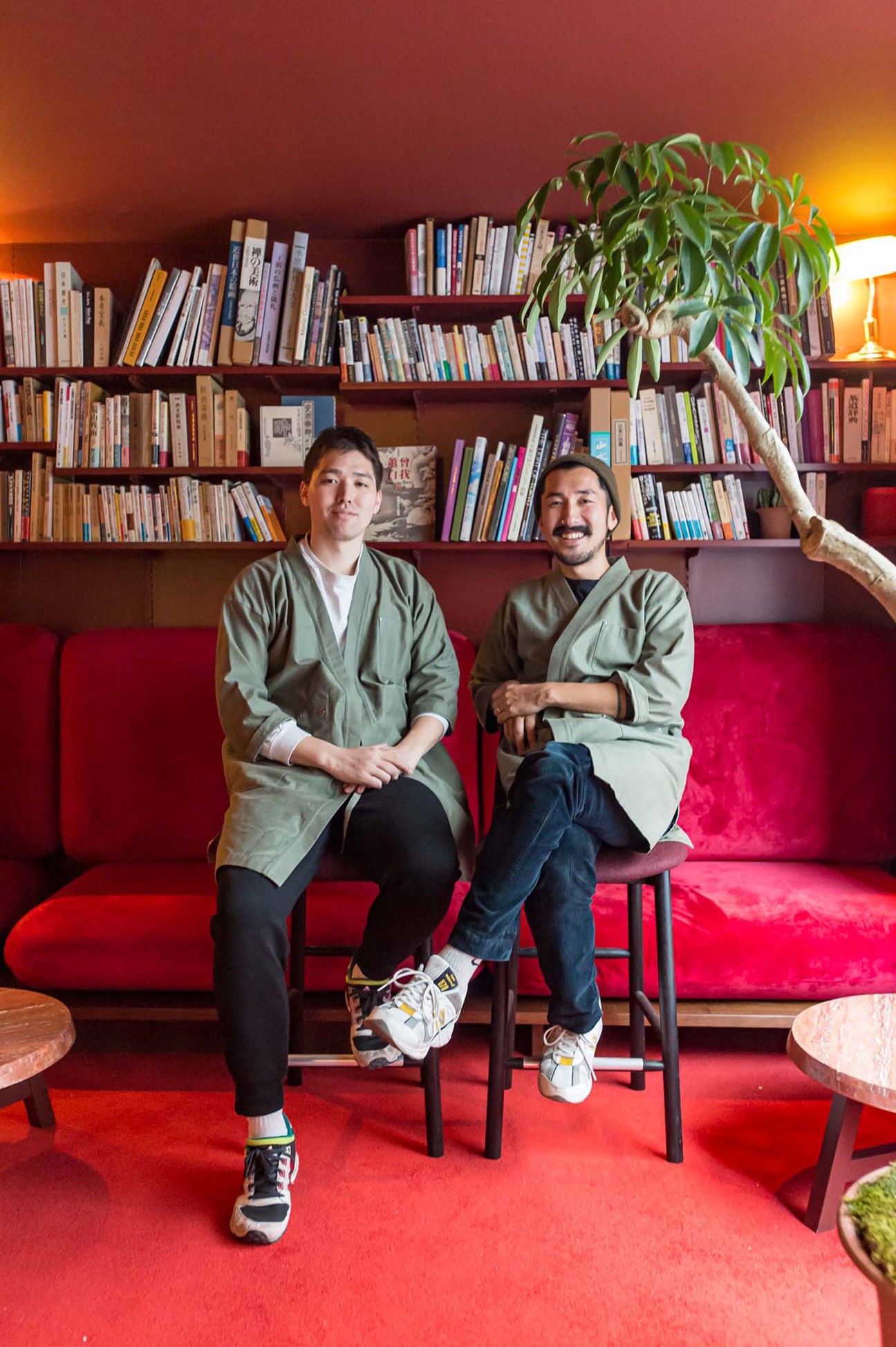 Kai Tanaka and Soran Nomura sitting on red chairs in front of bookshelves in Ao bar