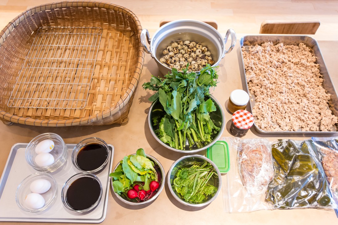 Overhead view of fresh ingredients laid out for cooking including eggs, quail eggs, vegetables, minced chicken, and Asian greens.
