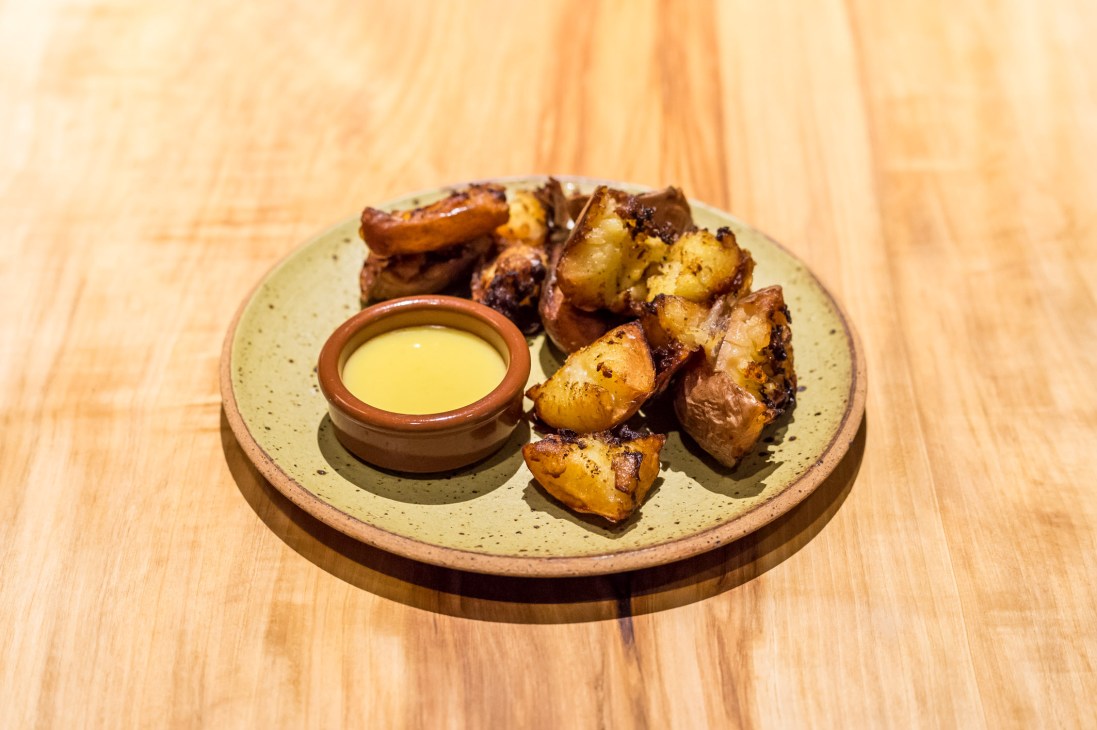 Fried potatoes with citrus mayonnaise served on a speckled ceramic plate with a small dish of pale yellow sauce.