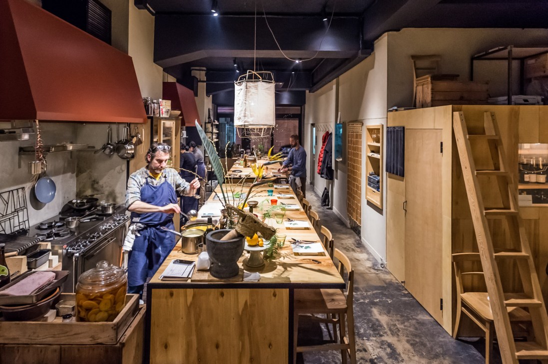 Chef working at wooden kitchen counter in The Blind Donkey restaurant with prep ingredients and hanging lantern.