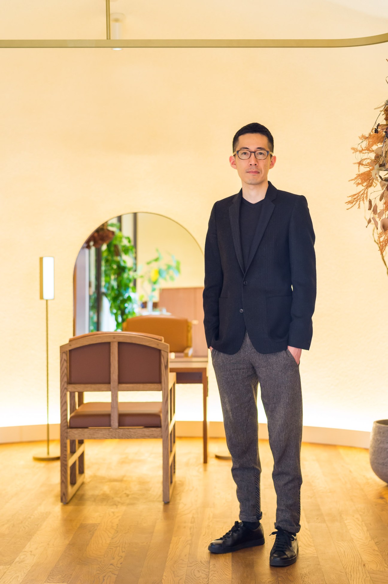 Architect Ryo Matsui standing in a minimalist salon interior with warm lighting and wooden flooring.