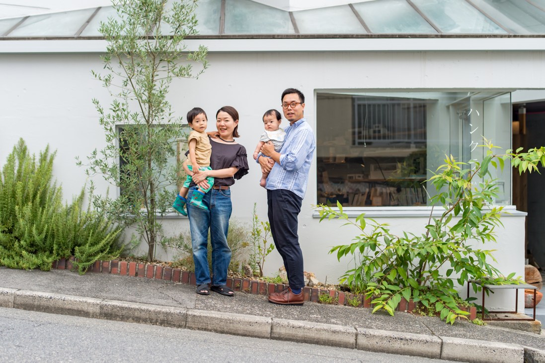 Sumire and Masafumi Shimatani with their two children standing outside their modern white home.