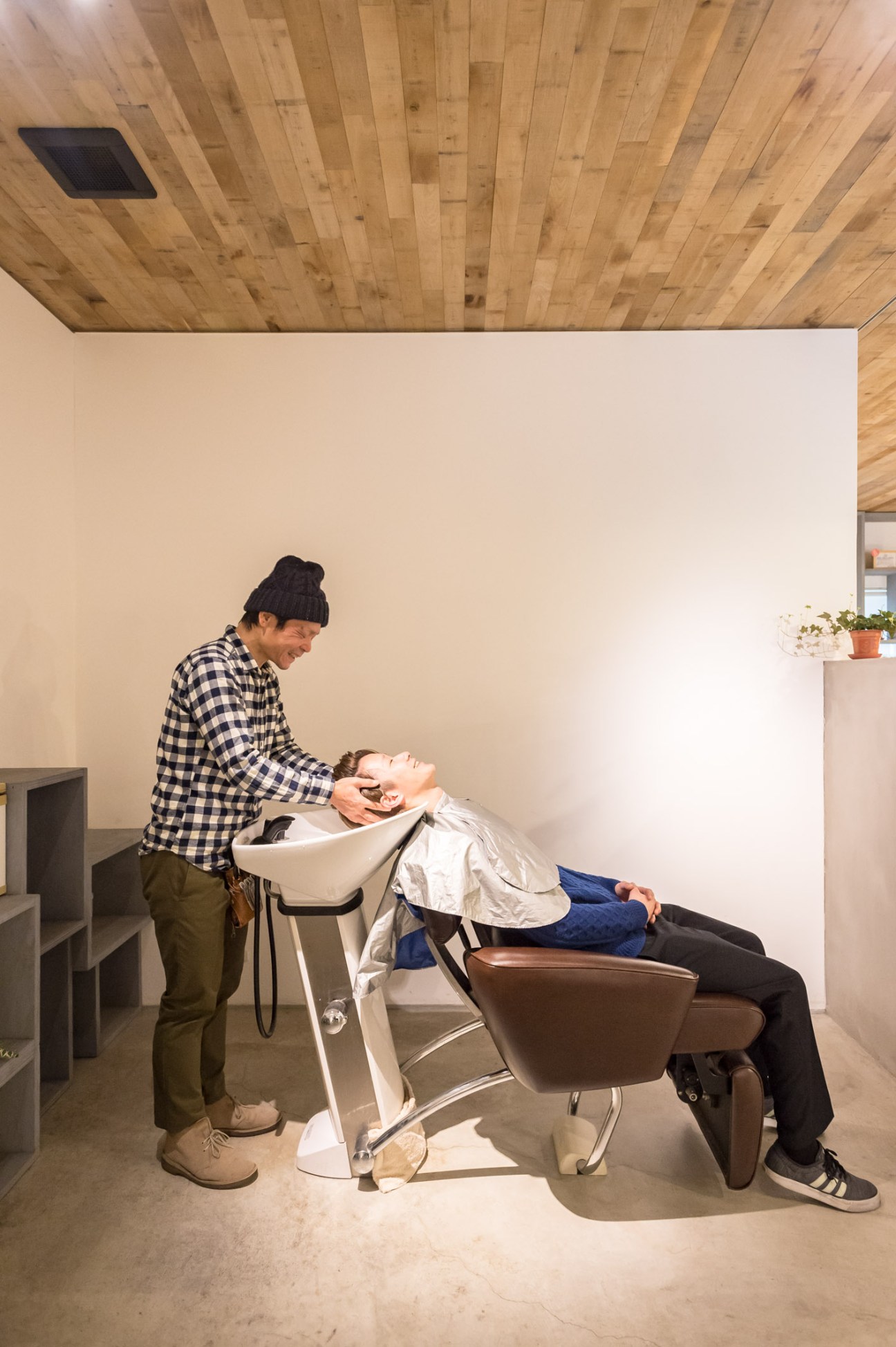 Hairdresser Kunihiro Murota cuts a client's hair in the minimalist Mook salon with oak-lined ceiling and cream walls.